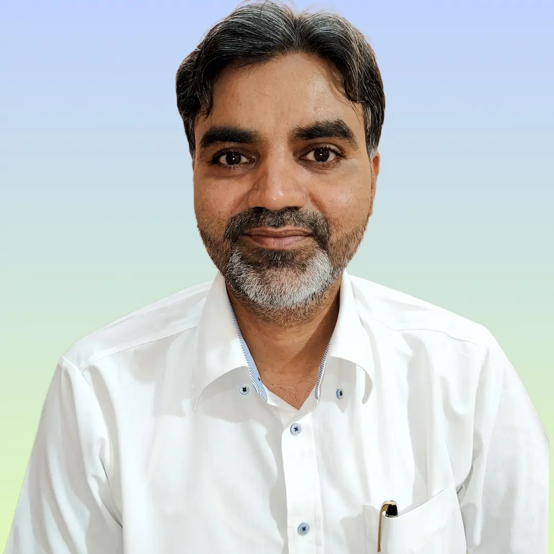 हसन बाबू सफेद शर्ट में कैमरे की तरफ देखते हुए हल्की मुस्कान के साथ